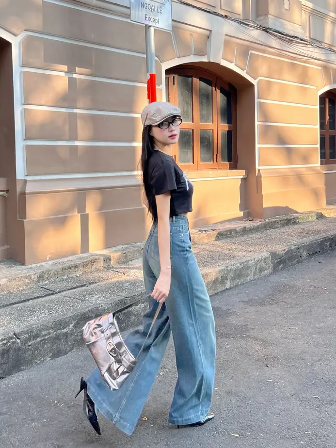Stylish woman in wide-leg flare jeans confidently walking with an urban cityscape behind her.